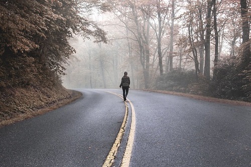 Pessoa caminhando no meio de uma estrada na natureza durante um dia de nevoeiro