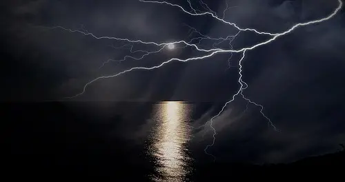 Fotografia de um relâmpago no céu com o mar e lua